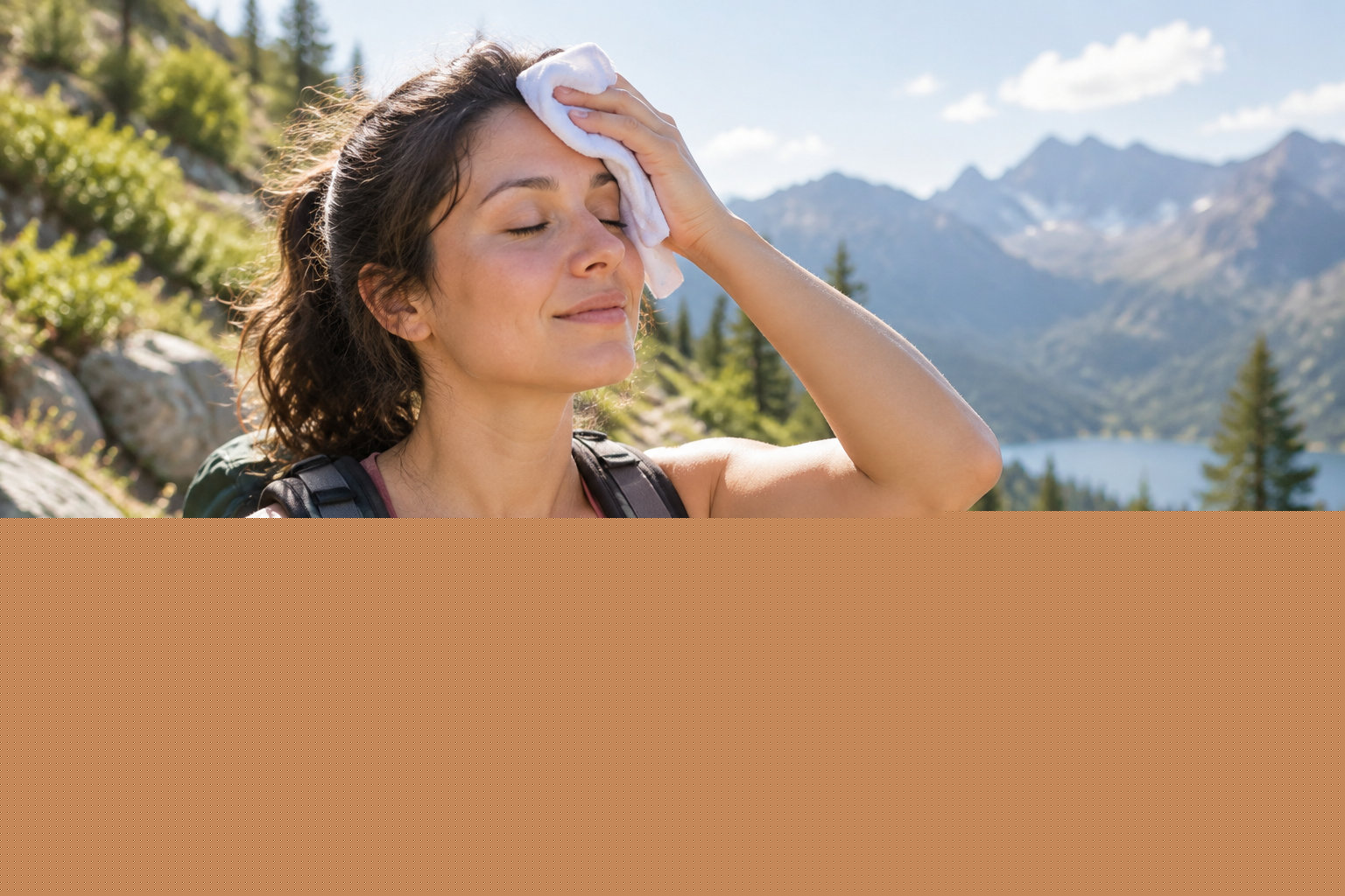 A woman wearing a backpack wipes her forehead with a cloth on a sunny mountain trail, with a lake and mountains in the background.